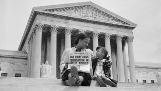 Nettie Hunt, sitting on steps of the Supreme Court in 1954, holding a newspaper and explaining to her daughter Nikie the meaning of the Court’s decision banning school segregation. (Photo/Bettmann Archive, Getty Images).