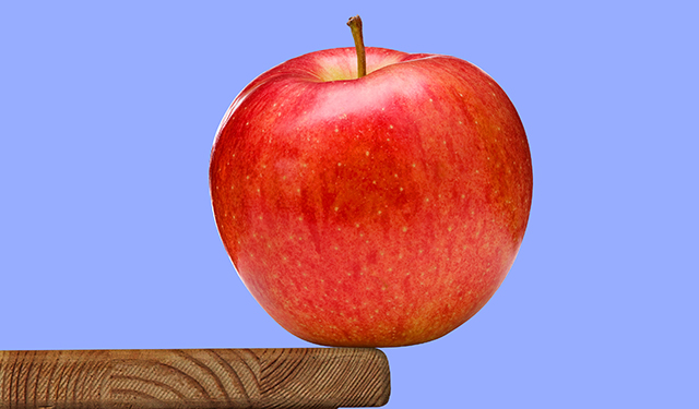An apple balances on the edge of a wooden desk.