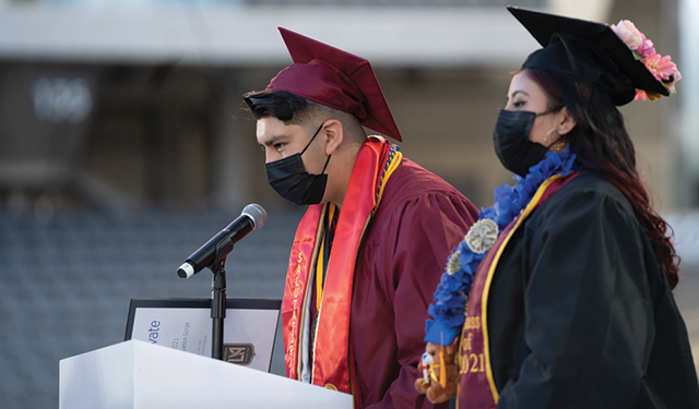 A high school student, dressed in a cap and gown, delivers a speech at graduation.