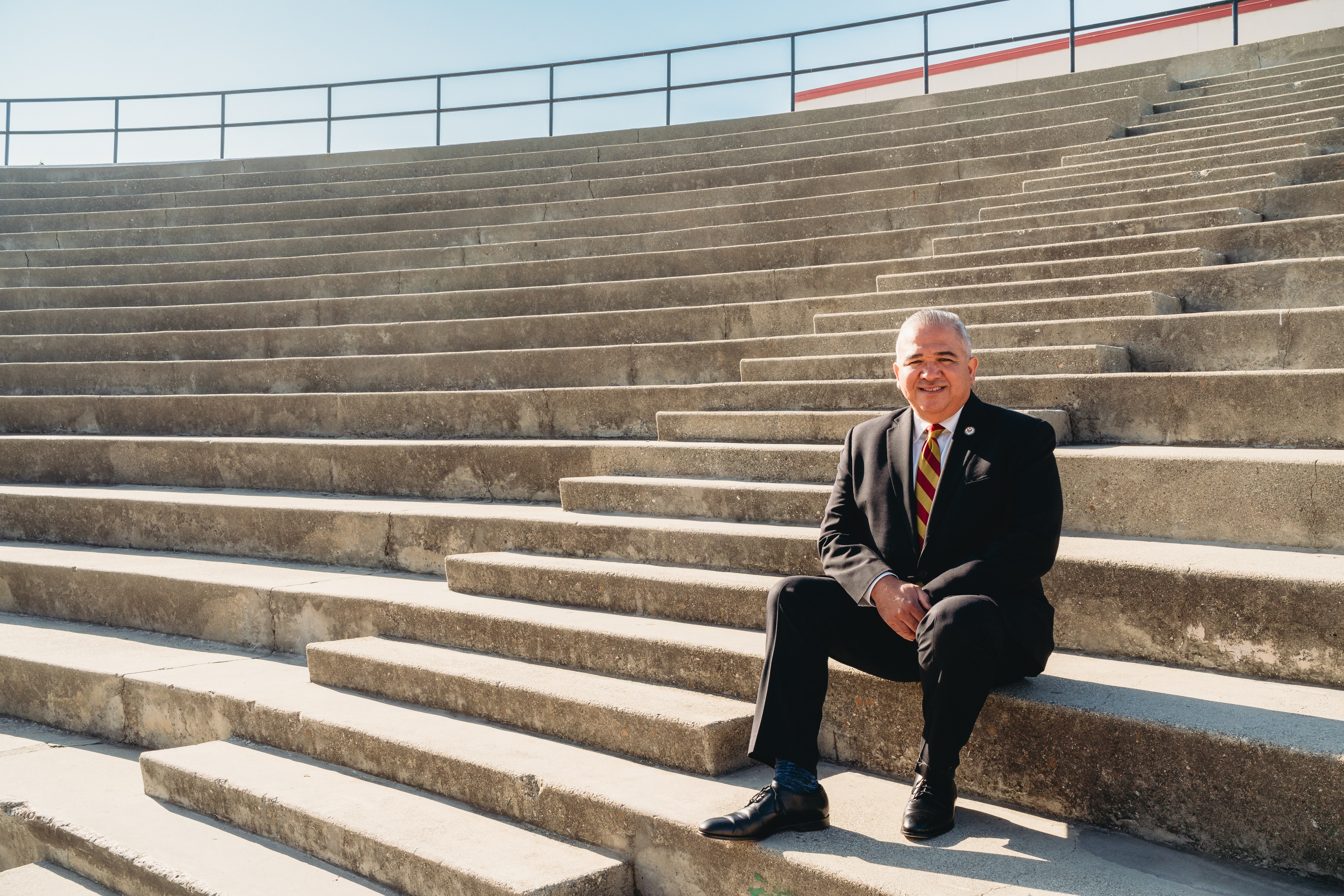 Portrait of Alfonso Jimenez sitting on the steps of a high school coliseum.