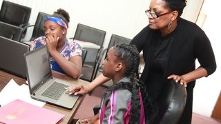A female instructor teaches two adolescent girls how to code on their laptops at Code Camp