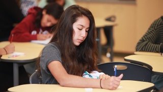 A young female student writes at her desk as schools and lawmakers debate mandating an ethnic studies course in K-12 schools