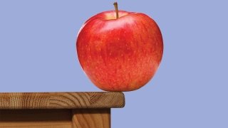 An apple balances on the edge of a wooden desk.