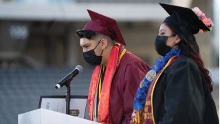 A high school student, dressed in a cap and gown, delivers a speech at graduation.