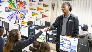 A college advisor bumps fists with a student as she works on a college applications on a desktop computer.