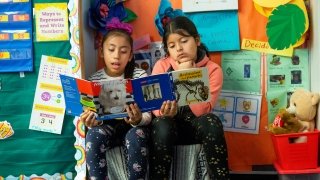 Two students read books side by side in an elementary school classroom.
