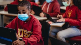 A young student in a cardinal and gold USC sweatshirt works at a laptop.