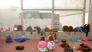 Two kindergarteners read together amid their classmates’ backpacks during an after-school program.