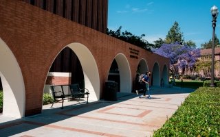 A student exists Waite Phillips Hall on a scooter.