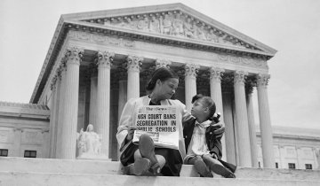 GettyImages-517350944-1160.jpg Nettie Hunt, sitting on steps of the Supreme Court in 1954, holding a newspaper and explaining to her daughter Nikie the meaning of the Court’s decision banning school segregation. (Photo/Bettmann Archive, Getty Images).