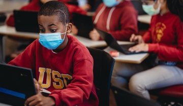 A young student in a cardinal and gold USC sweatshirt works at a laptop.