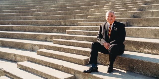 Portrait of Alfonso Jimenez sitting on the steps of a high school coliseum.