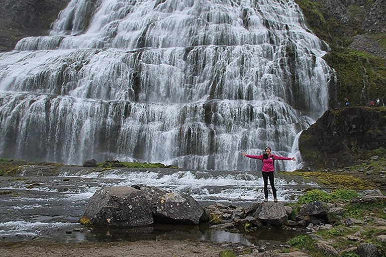 Laura Chase, MAT '15, a teacher, stands next to a large Arctic waterfall