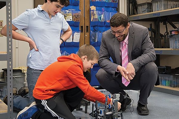 Elias Miles, Superintendent, crouches down near a student to review a class project