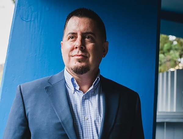 Elias Vargas, School Director, poses for a photo in front of a blue backdrop