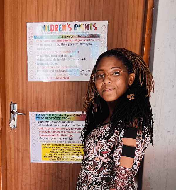 Cymone Davis poses for a photo in front of a sign in a classroom displaying "Children's Rights," adapted from South Africa's Bill of Rights.