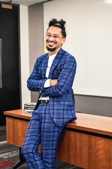 Photograph of Josh Schuschke wearing a blue plaid suit and teaching in a classroom.