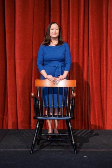 Photo of Tracy Poon Tambascia standing behind a chair.