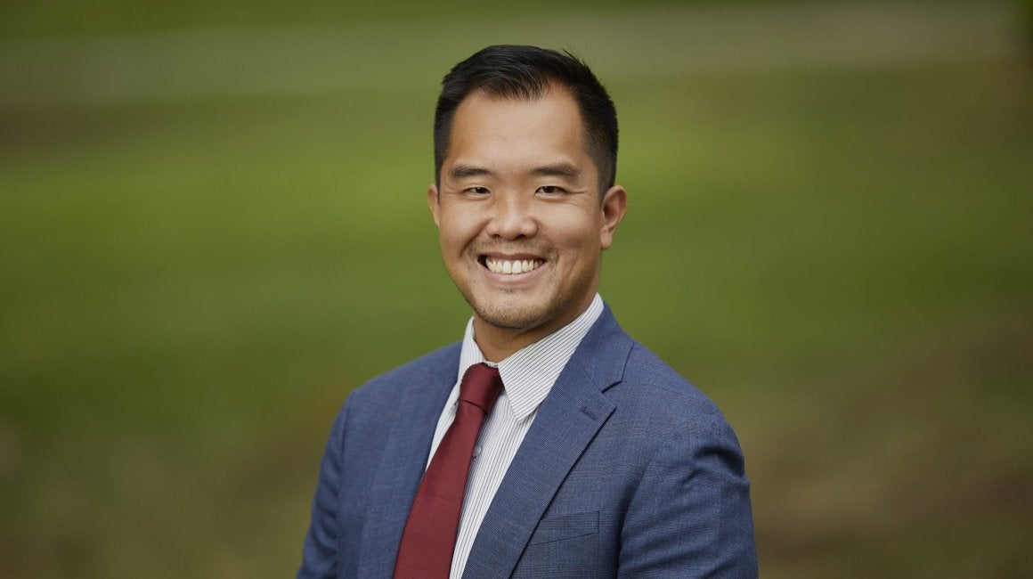 Headshot portrait of Federick Ngo smiling in a blue suit and red tie outdoors