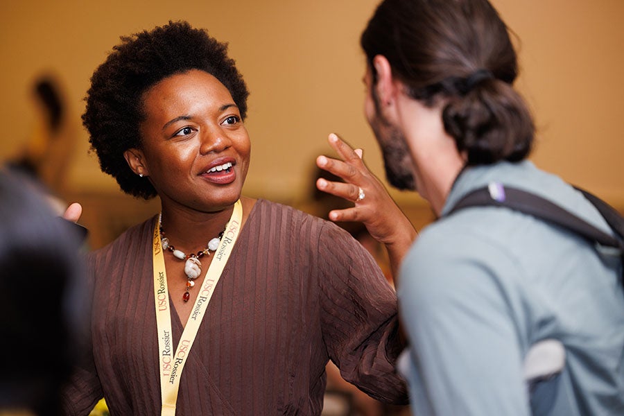 Two attendees in conversation at a USC Rossier conference, one wearing a USC Rossier lanyard