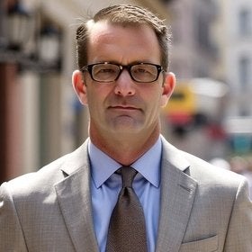 Portrait of Eric Canny in a tan blazer and tie on a city street