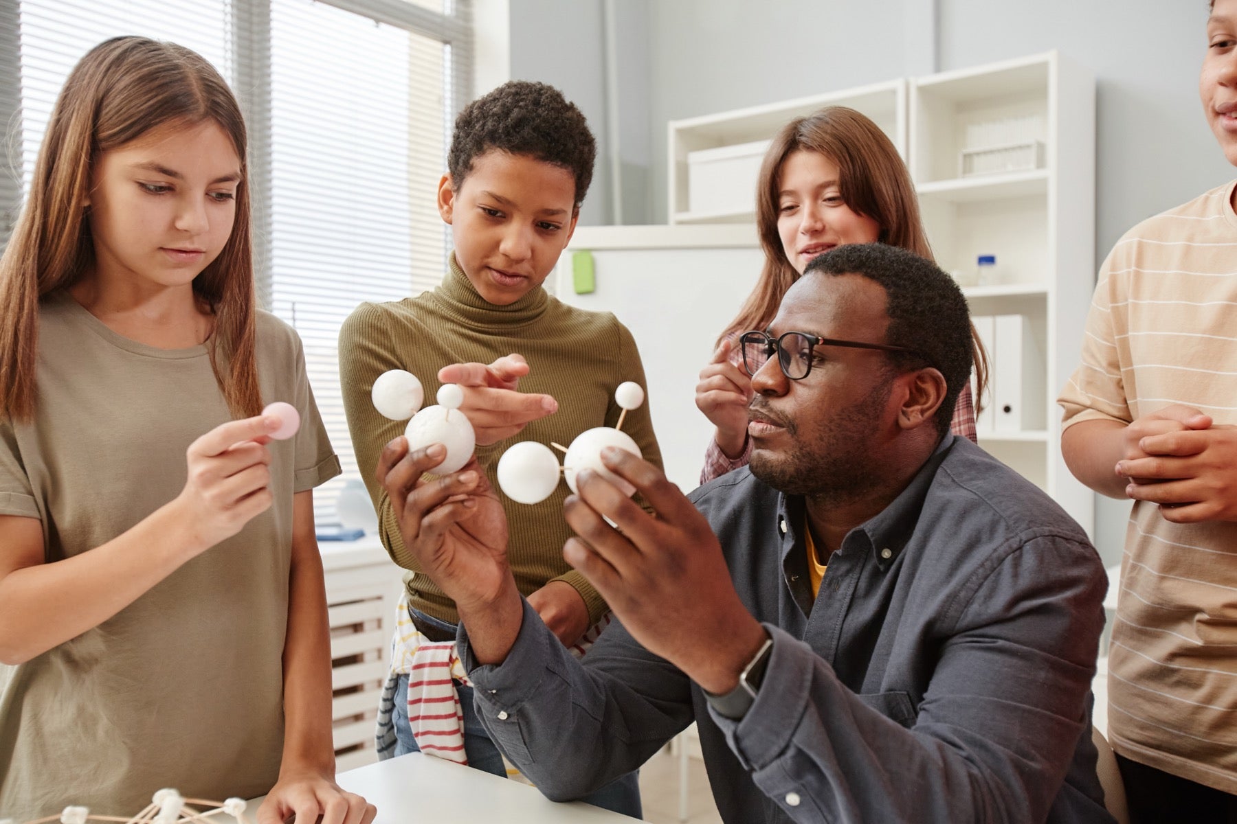 Teacher showing students a molecule model made of foam balls in a science classroom