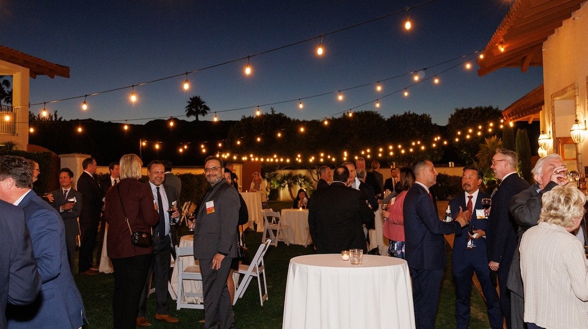 Guests mingling at an outdoor evening reception with string lights and cocktail tables