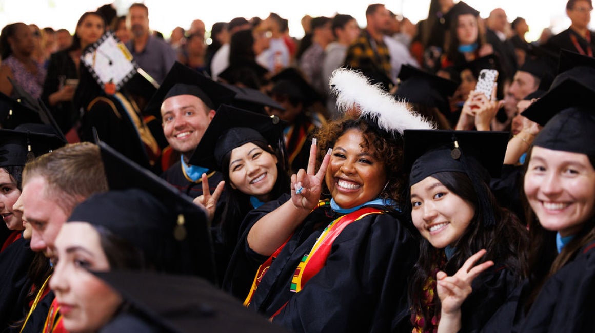 Graduates in caps and gowns smiling and making peace signs at a commencement ceremony