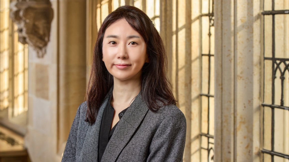 Headshot portrait of Cheyeon Ha smiling in a plaid blazer indoors