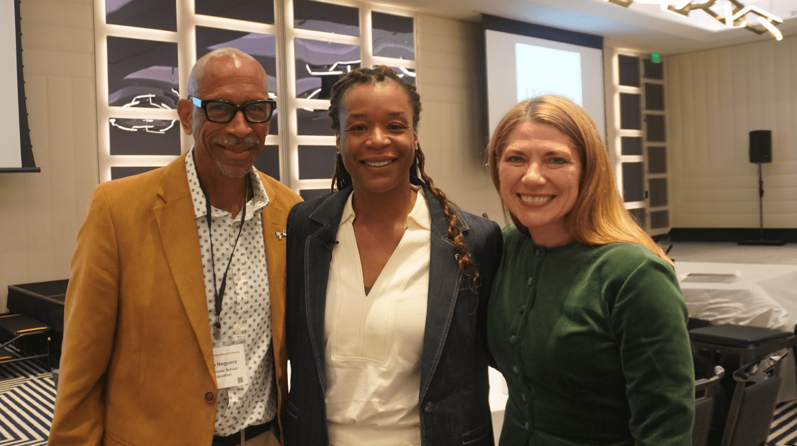 Three people smiling together indoors at a conference