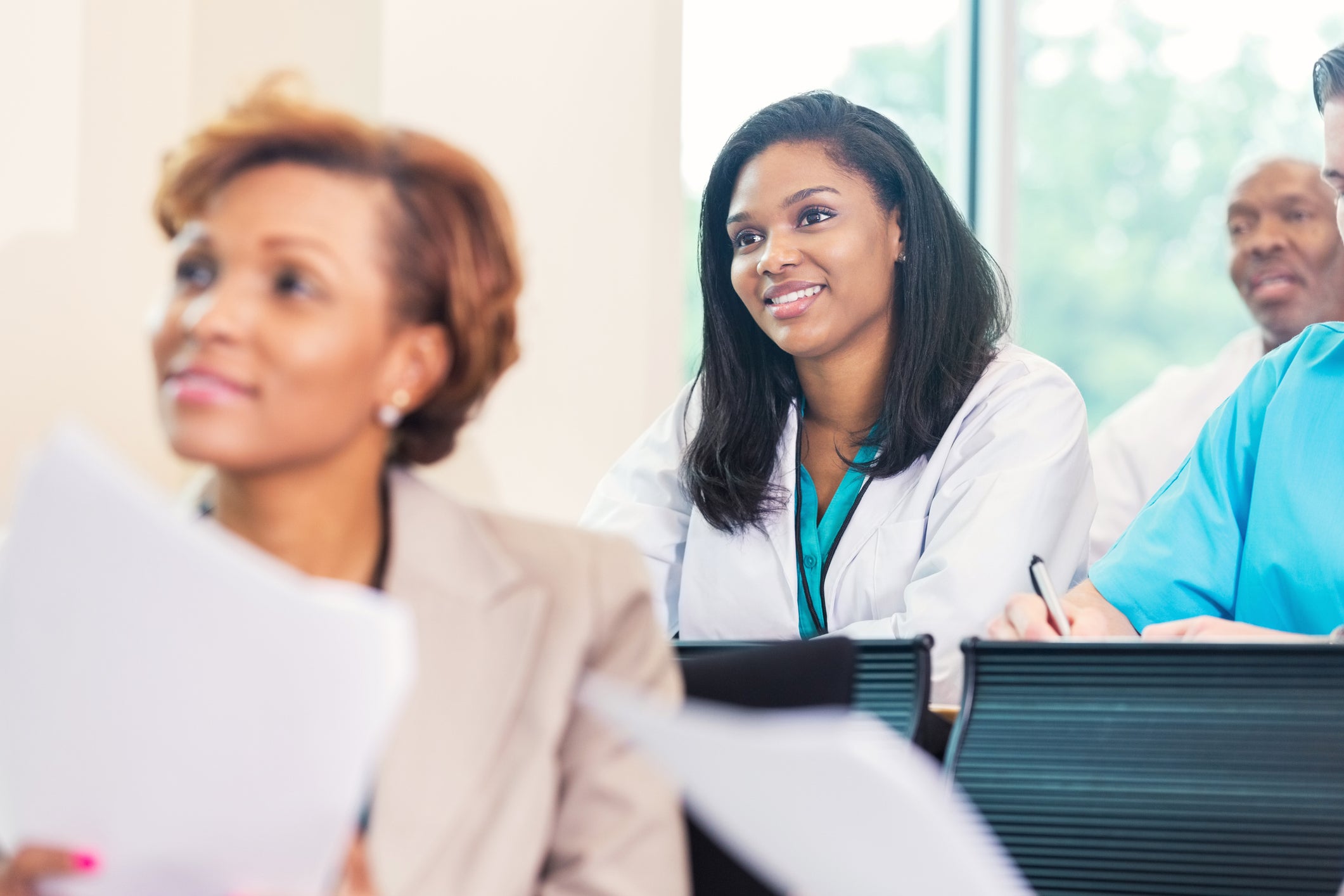 Woman in a lab coat smiling while seated in a lecture audience