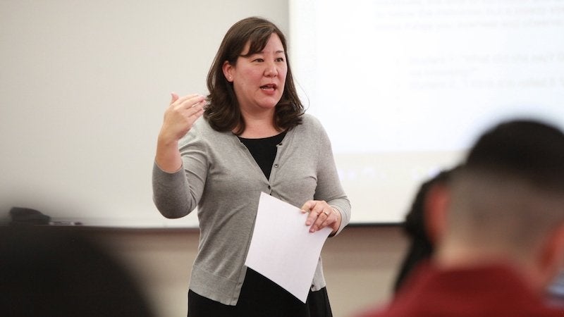 Kimberly Hirabayashi gesturing while speaking to a classroom holding papers