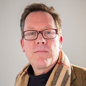 Portrait of Lynch wearing glasses and a plaid scarf