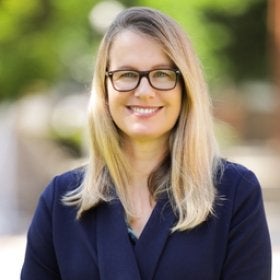 Headshot portrait of Seli smiling outdoors in a navy blazer