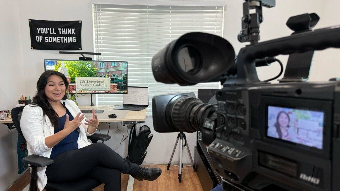 Woman being filmed for a television interview with USC branding shown on a monitor
