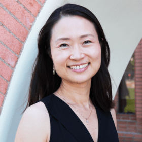 Headshot portrait of Yang smiling outdoors near brick archways