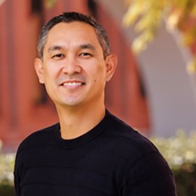 Headshot portrait of Atheneus Ocampo smiling outdoors near brick archways