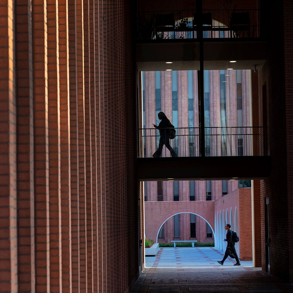 Silhouette of a person walking across an elevated walkway in a modern brick campus building