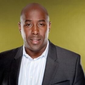 Headshot portrait of Darnell Cole in a dark suit against a yellow-green background