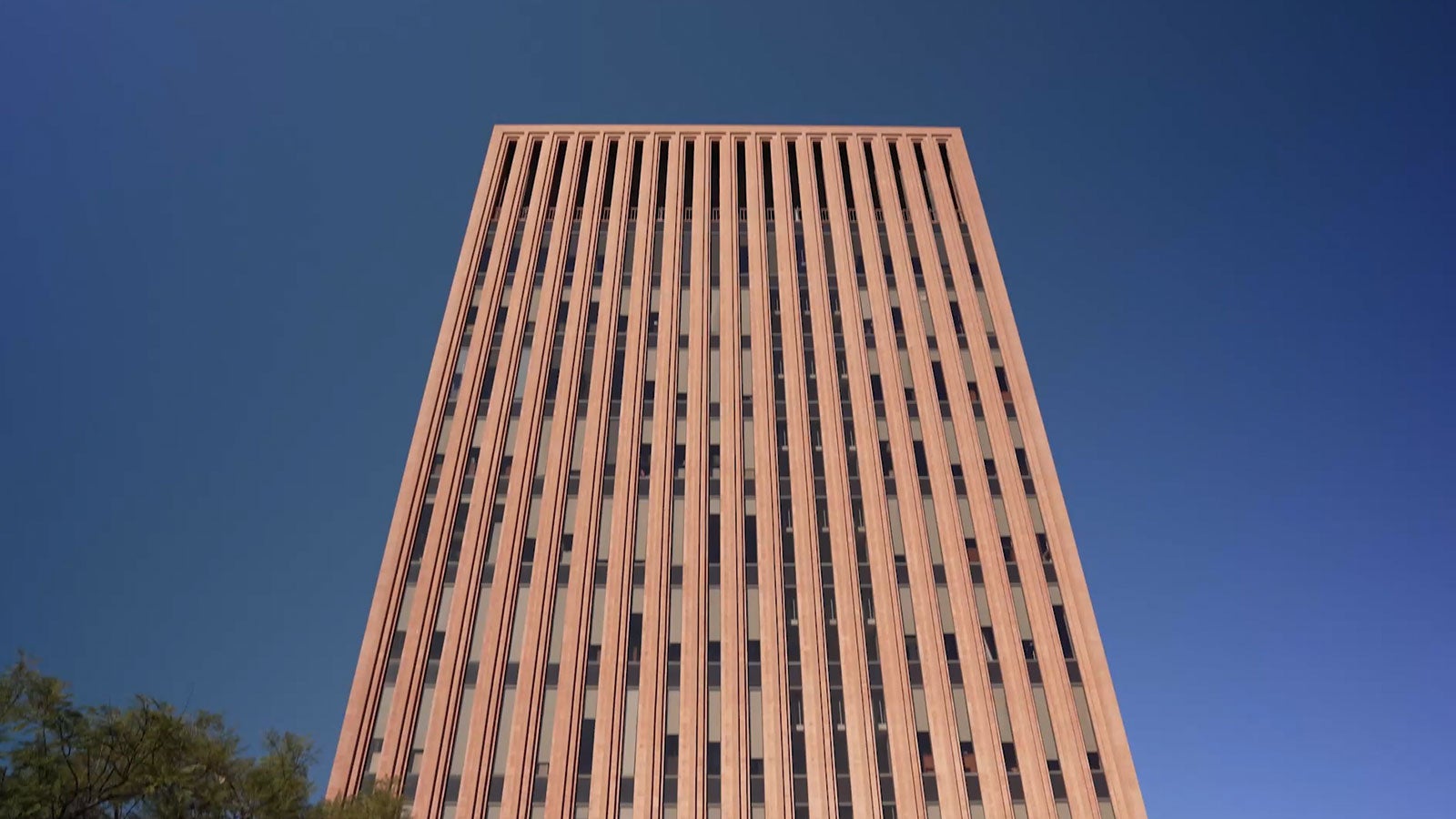 Low-angle view of a tall brick university tower against a clear blue sky