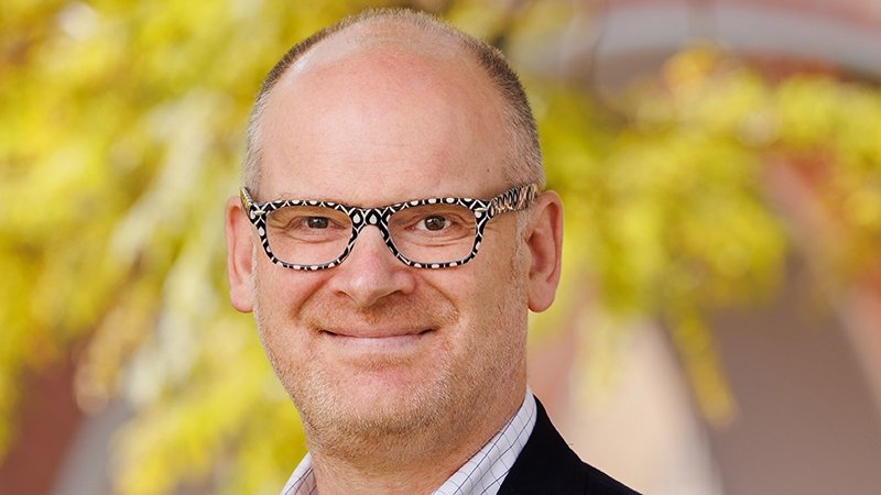 Headshot portrait of a smiling man wearing patterned glasses outdoors
