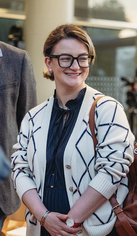 Woman smiling outdoors while wearing glasses and a patterned cardigan