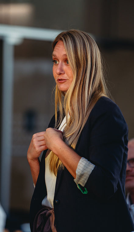 Woman speaking outdoors during golden hour, wearing a dark blazer