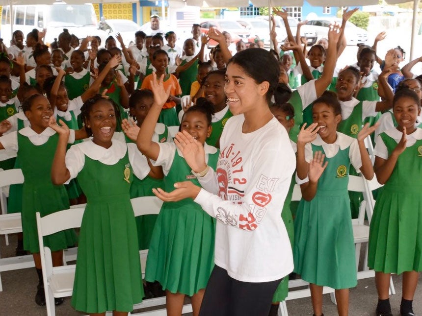 A woman high-fiving a cheering group of schoolchildren in green uniforms outdoors
