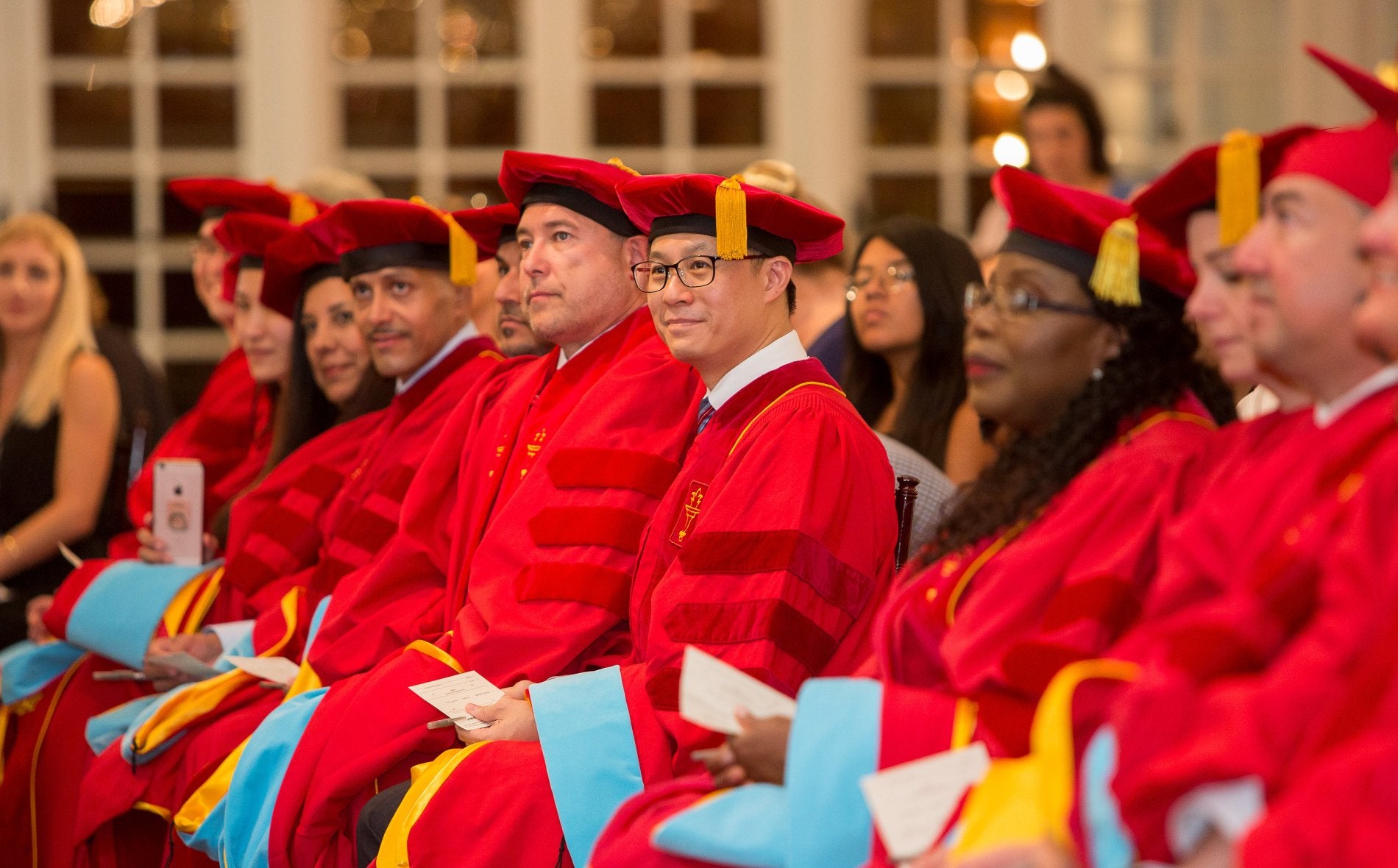 Doctoral graduates seated in red robes and caps with gold tassels during a Global EdD commencement ceremony