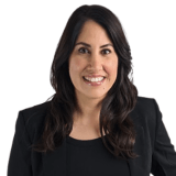 Headshot portrait of Delia smiling in a black blazer against a white background