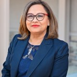 Headshot portrait of a smiling woman in glasses and a navy blazer