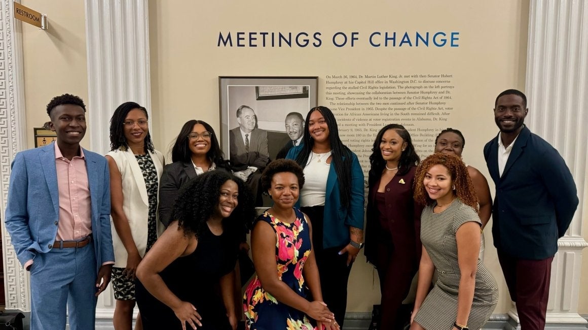 Group of students and staff smiling together beneath a 'Meetings of Change' civil rights exhibit display