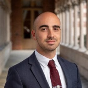 Headshot portrait of Jacob Alonso smiling in a suit near a campus archway