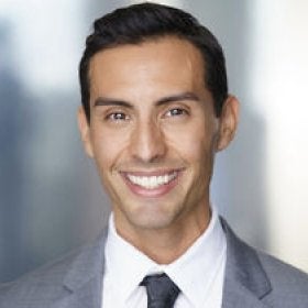 Headshot portrait of Marcus smiling in a gray suit and tie